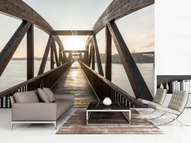 Fototapete Brücke über den Fluss – urbane Architekturlandschaft mit einer Holzbrücke über dem Fluss und der Sonne im Hintergrund